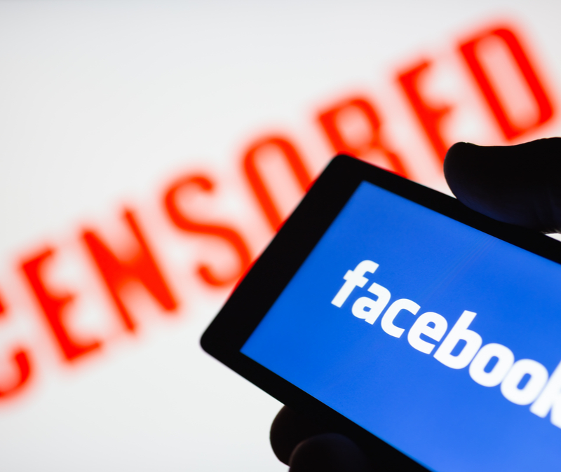 Facebook logo on handheld smartphone with banner reading censored
