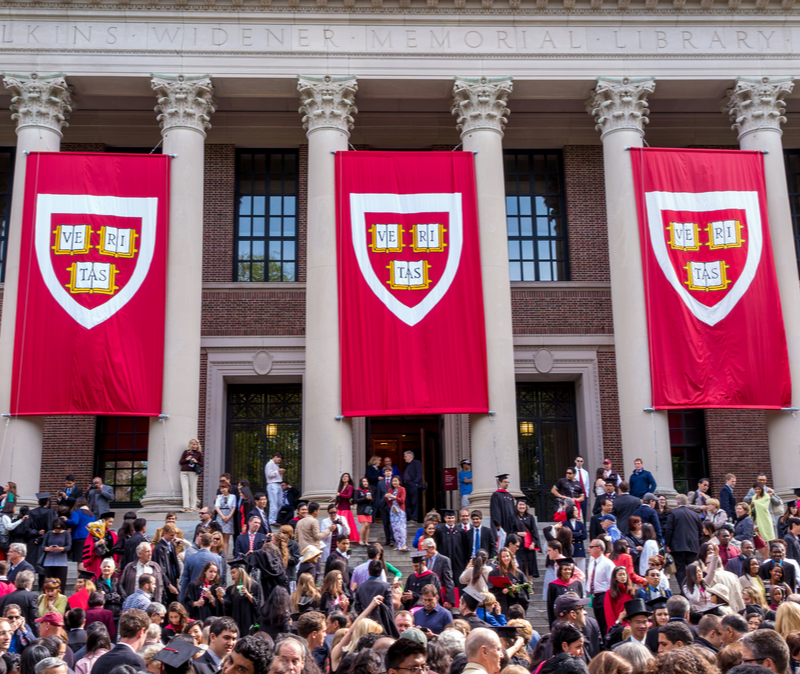 crimson banners hang over steps crowded with Harvard students